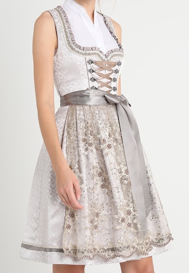Femme portant une robe traditionnelle sans manches avec un corsage à lacets, un chemisier blanc et un tablier brodé de fleurs noué avec un large ruban en satin.
