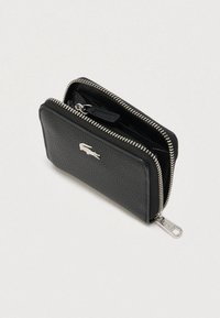 Cartera con cremallera de cuero negro texturizado con cierre plateado y logotipo de cocodrilo, parcialmente abierta mostrando los compartimentos interiores.