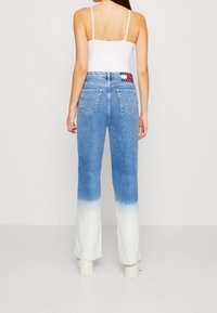 Nainen, joka on pukeutunut sinivalkoisiin ombre-suoraraitapantseihin ja valkoiseen napakkaan topiin, seisoo selkä kameraan päin.