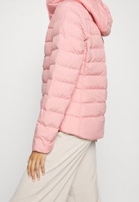Veste doudoune rose avec un design matelassé, dotée d'une capuche et de manches longues, fabriquée en tissu lisse et léger.
