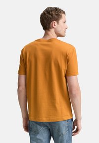 Sennepsgul t-shirt med korte ærmer og en struktureret, ribbet overflade. Rund halsudskæring, afslappet pasform, båret med lyseblå jeans.