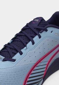 Αθλητικό παπούτσι σε ανοιχτό γαλάζιο και ναυτικό μπλε με κορδόνια σε σκούρο μωβ, ροζ και μαύρες λωρίδες διακόσμησης, και υλικό επάνω μέρος με υφή που επιτρέπει την αναπνοή.