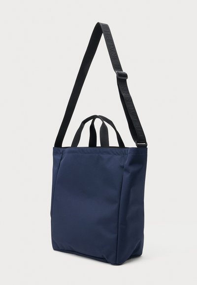 Sac cabas bleu marine avec deux poignées courtes et une sangle d'épaule noire réglable sur fond blanc.