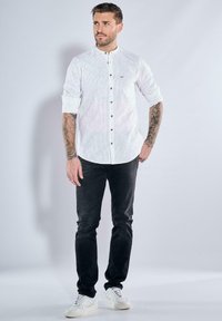 Weiß gestreifte Hemd mit Stehkragen, kombiniert mit schwarzen Jeans und weißen Sneakers, bietet einen lässigen Schnitt und strukturierten Stoff.