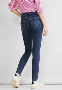 Jeans ajustados de denim azul oscuro, con cintura alta, bolsillos traseros y un corte ajustado. Combinados con zapatillas blancas y una camiseta a rayas rosa.