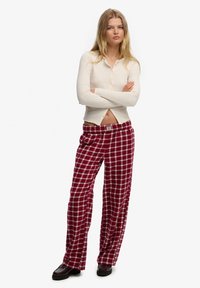 Długie, luźne spodnie w kratę w kolorze bordowym i białym, wykonane z miękkiego materiału, zestawione z kremowym, prążkowanym topem z długim rękawem z zapięciem na guziki.