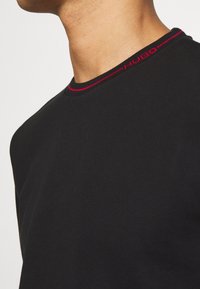 Schwarzes Kurzarm-T-Shirt mit runder Ausschnittkante und kontrastierender roter Naht sowie 'HUGO'-Logodetail. Weicher Stoff, taillierte Passform.