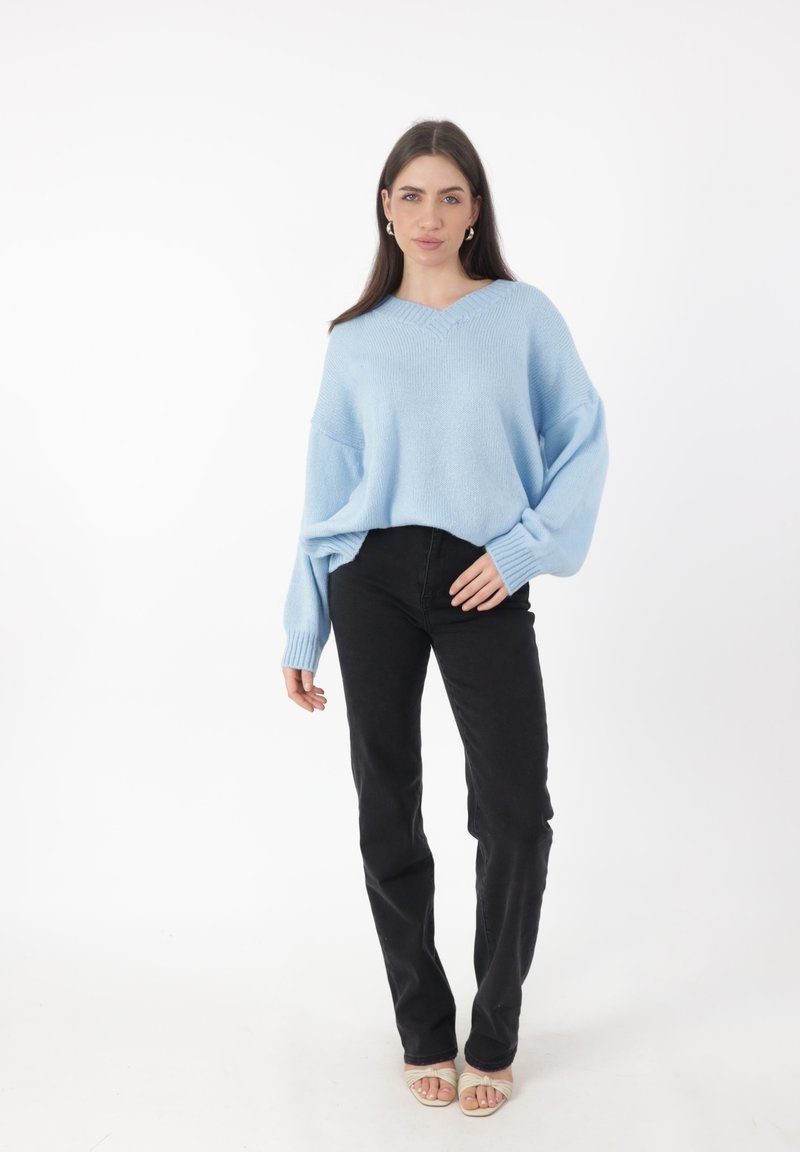 Hellblaues, oversized Sweatshirt mit V-Ausschnitt, gerippten Bündchen und lockerer Passform, kombiniert mit schwarzen geraden Jeans und offenen Sandalen.