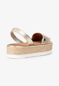 Sandalias slingback doradas metálicas con plataforma de esparto trenzada, parte superior texturizada y suela de goma blanca. Diseño sencillo y altura moderada.