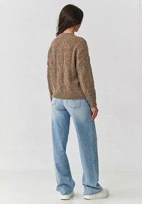 Brązowy sweter dzianinowy o teksturowanym wzorze, w zestawieniu z jasnoniebieskimi spodniami typu wide-leg i białymi trampkami, widok od tyłu.