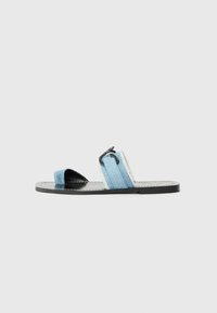 Blue denim slide sandals with black sole, featuring two wide straps and a distinctive clip accent on the strap. Flat design and open-toe style.