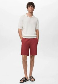Bílá, texturovaná polokošile s krátkým rukávem v kombinaci s burgundskými kraťasy po kolena. Černé sandály doplňují neformální outfit.