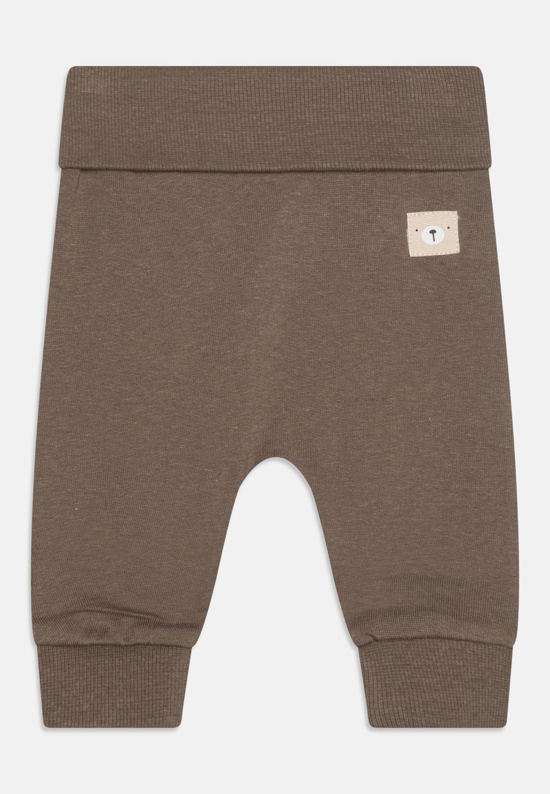 Pruuni puuvillased püksid ribakujulise vöökoha ja mansettidega, millel on väike beežipatch karu näo detailiga. Pehme tekstuur, kitsenev disain.