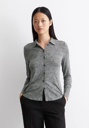Black and white patterned long-sleeve shirt with a button-down front, spread collar, and black buttons, paired with black trousers.