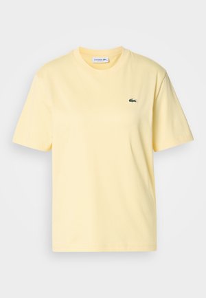 T-shirt de algodão amarelo com mangas curtas e decote redondo. Apresenta um pequeno logótipo de crocodilo bordado em verde no peito.