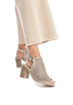 Sandales ouvertes beige avec design perforé, bride de cheville, talon carré et finition texturée semblable au bois, sur fond blanc.