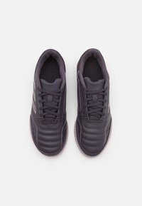 Zapatillas deportivas de color púrpura oscuro con una parte superior acolchada, tela texturizada y detalles de costura. Presenta cordones en bucle y una suela de goma.