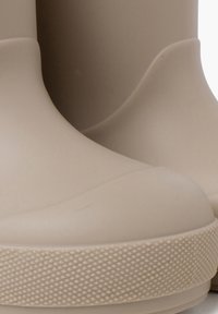 Botas de goma beige con un acabado suave, punta redondeada y suela texturada. Labio ligeramente elevado en la parte superior para facilitar su uso.