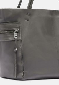 Borsa a tracolla in pelle grigia caratterizzata da una tasca con zip, texture liscia e dettagli di cucitura minimal. La borsa ha manici robusti per il trasporto.