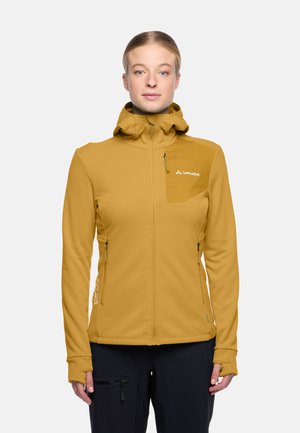 Gelbe Softshelljacke mit Kapuze, Reißverschluss-Taschen und Daumenlöchern. Hat ein tailliertes Design und ein Logo auf der Brust.
