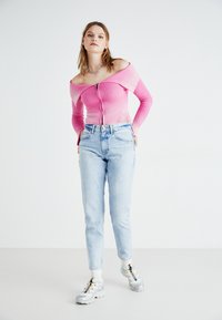 Top rosa de canalé con hombros al descubierto y cremallera delantera, combinado con jeans de pierna recta de color azul claro y zapatillas plateadas con acentos coloridos.