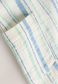 Manchette avec des rayures horizontales bleu clair et vert sur un tissu blanc texturé.