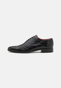 Scarpa in pelle nera con motivo testurizzato in pelle di coccodrillo. Caratterizzata da un design con lacci, punta arrotondata e una sottile suola in gomma.