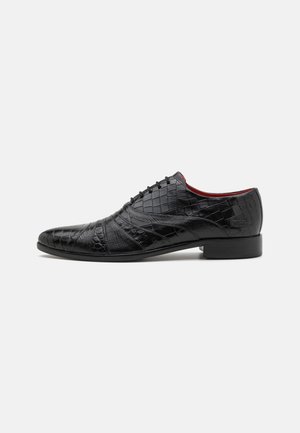 Scarpa in pelle nera con motivo testurizzato in pelle di coccodrillo. Caratterizzata da un design con lacci, punta arrotondata e una sottile suola in gomma.