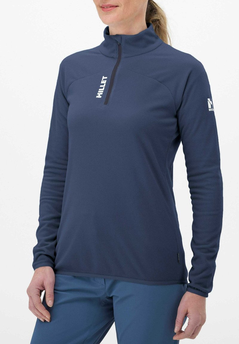 Pull à col zippé en bleu marine à manches longues. Confectionné dans un tissu texturé avec un logo sur la poitrine et la manche. Finition lisse, matériau respirant.