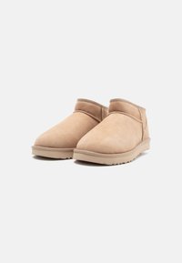 Beige Wildlederschuhe mit rundem Zeh, gepolstertem Kragen und strukturiertem Gummisohle. Einfaches Design mit minimalen Nähdetails.