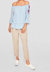 Top azzurro chiaro off-the-shoulder con maniche a tre quarti a campana, orlo peplum e ricami floreali bordeaux sulle maniche. Abbinato a pantaloni beige.