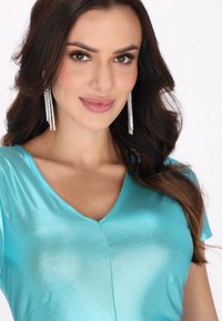 Turkoosi satiinipaita lyhyillä hihoilla, V-pääntiellä ja hienovaraisella kiillolla. Ominaisuuksiin kuuluu siisti leikkaus ja sileä pinta. Kimaltavat hopeakorvakorut korostavat ilmettä.