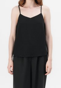Top in camicia nera con sottili spalline regolabili, scollatura a V e un tessuto leggero e fluido, adatto per un look a strati o per un abbigliamento casual.