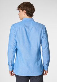 Camicia a maniche lunghe azzurro chiaro con colletto button-down, texture morbida e orlo arrotondato. Presenta polsini con bottoni e un yoke posteriore.