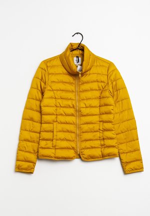 Gul quiltet jakke med lynlås foran og høj krave, hængende på en sort bøjle mod en hvid baggrund.
