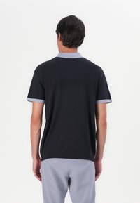 Polo de manga curta em azul-marinho escuro com colarinho e punhos em azul-claro. Apresenta riscas verticais texturizadas nas costas.