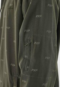 Giacca in tessuto verde con un sottile motivo PXP logo su tutta la superficie, tasca laterale sulla manica e texture liscia.