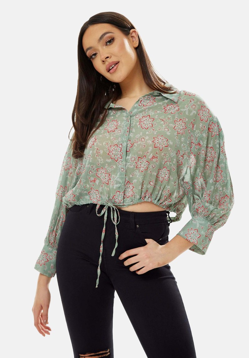 Light green, floral-patterned cropped blouse with a button-up front, collar, and gathered sleeves, featuring a tie closure at the waist.