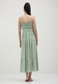 Light green, ankle-length dress with a smocked bodice and spaghetti straps. Features a tiered design, soft texture, and a flowing silhouette.