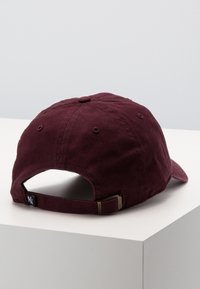 Gorra color marrón con una textura suave de algodón, visera curva, correa trasera ajustable y un logo en la parte posterior. Diseño simple con agujeros de ventilación.