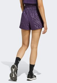 Lila Sportshorts mit einem strukturierten Muster, elastischem Bund und seitlichen Schlitzen für Bewegungsfreiheit, kombiniert mit schwarzen Knöchelsocken und Sneakers.