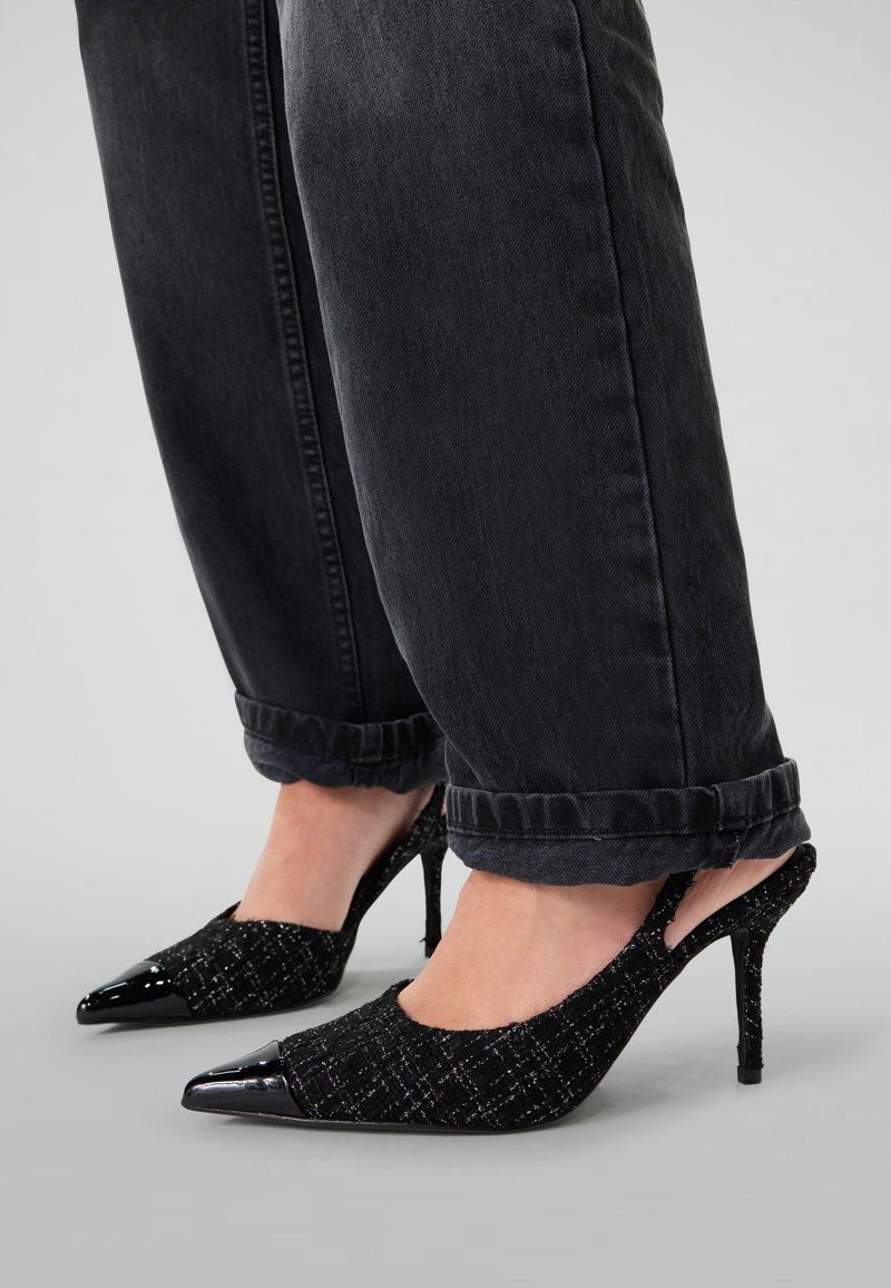 Escarpins noirs avec une bride arrière en tissu texturé et un bout en verni noir brillant. Ils ont un bout pointu et un talon aiguille fin.