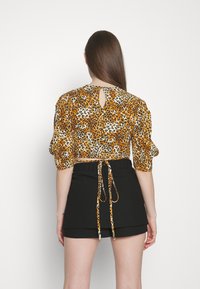 Blouse courte en imprimé léopard dans des tons orange, noir et crème, avec des manches bouffantes et un détail en keyhole à l'arrière, associée à une mini jupe noire.