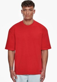 Camiseta de manga corta roja, hecha de algodón, con un corte relajado y cuello redondo. Sin patrones ni diseños, de color liso, con etiqueta en el dobladillo.