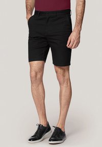 Czarne bawełniane szorty o prostym kroju, z przednimi kieszeniami i zapięciem na guziki. Noszone z czarnymi sneakersami z białymi podeszwami.