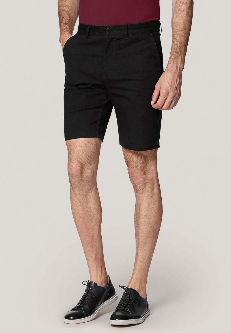 Czarne bawełniane szorty o prostym kroju, z przednimi kieszeniami i zapięciem na guziki. Noszone z czarnymi sneakersami z białymi podeszwami.