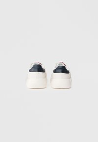 Hvide sneakers med en glat, læderoverdel, marineblå hælaccenter og en struktureret sål. Minimalistisk design med diskret branddetalje.