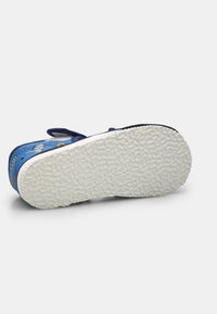 Sinine laste king, millel on valge tekstureeritud põhi, suunatud ülespoole, koos multikaraktäride mustrite ja Velcro rihmaga valgel taustal.