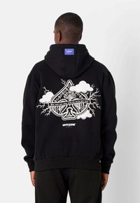 Sudadera negra con una gran gráfica blanca que presenta un símbolo de as, rayos y nubes en la parte posterior. Puños y cinturilla acanalados.
