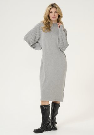 Graues Strickkleid mit gerippten Puffärmeln. Glatte Stoffqualität, knielang, kombiniert mit schwarzen kniehohen Stiefeln mit Schnallen und einem klobigen Absatz.